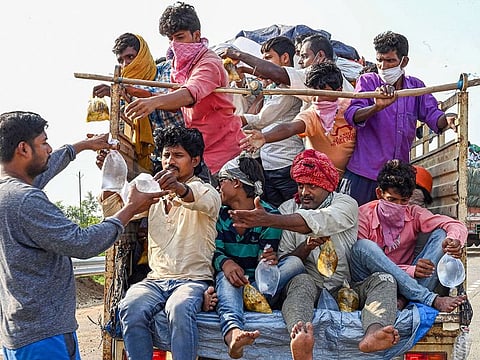 A volunteer distributes drinking water as migrants board a tempo to travel to their native places, during the ongoing COVID-19 nationwide lockdown, in Jabalpur, on May 17, 2020.
