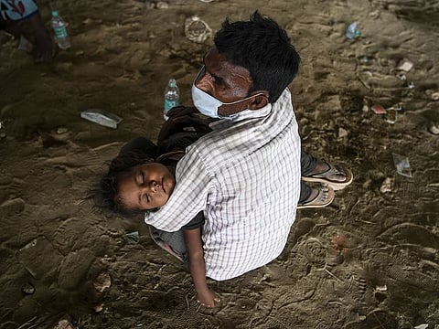 A migrant worker holds a child resting on his lap as he waits with others for transport to return to their hometowns in Uttar Pradesh after police stopped them from crossing the Delhi-Uttar Pradesh border on foot.