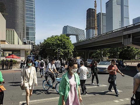Pedestrians wearing protective masks cross a road near the China Central Television (CCTV) headquarters building, rear center, in Beijing, China, on Wednesday, May 20, 2020.