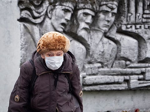 A woman wearing a face mask to protect against coronavirus walk past a Soviet era bas-relief in St. Petersburg, Russia, Thursday, May 21, 2020.