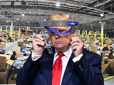 President Donald Trump looks through a face shield, in front of poster of the manufacturing of these shields, while touring Ford Motor Co.'s Rawsonville Components Plant in Ypsilanti, Michigan on Thursday, May 21, 2020.