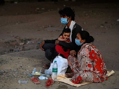 A migrant worker family with their three month old child wait under a flyover for transportation to get back to their village during a nationwide lockdown to curb the spread of new coronavirus in New Delhi, India.
