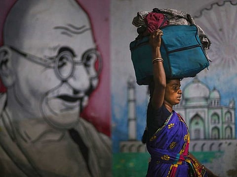 A migrant woman carries her belongings on her head as she walks past a wall painting of Mahatma Gandhi to board a train to her home state, at Hyderabad Railway Station in Hyderabad, India