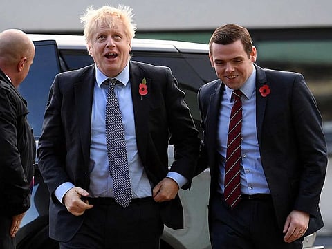 In this file photo taken on November 07, 2019 Britain's Prime Minister Boris Johnson (C) is greeted by Conservative party candidate for Moray, Douglas Ross (R) as he arrives for a general election campaign visit to Diageo's Roseisle Distillery near Elgin, north east Scotland. British Prime Minister Boris Johnson's government suffered its first resignation over the controversy surrounding senior aide Dominic Cummings' trip across country during coronavirus lockdown when Douglas Ross, a minister for Scotland, quit in protest on Tuesday.