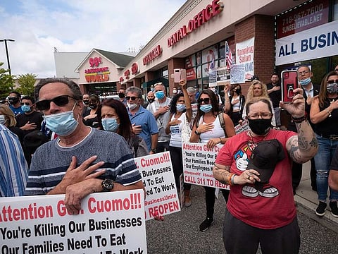 A crowd gives the Pledge of Allegiance while supporting Bobby Catone, the owner of a Staten Island tanning salon, Thursday, May 28, 2020, in New York. Catone opened the salon briefly Thursday morning in defiance of a law requiring non-essential businesses to remain closed during the coronavirus pandemic.