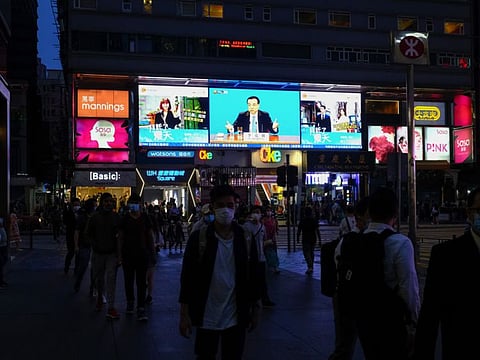 Pedestrians pass a screen showing a news broadcast of Chinese Premier Li Keqiang attending the National People’s Congress in Beijing, at night in Hong Kong, China, on Thursday, May 28, 2020.