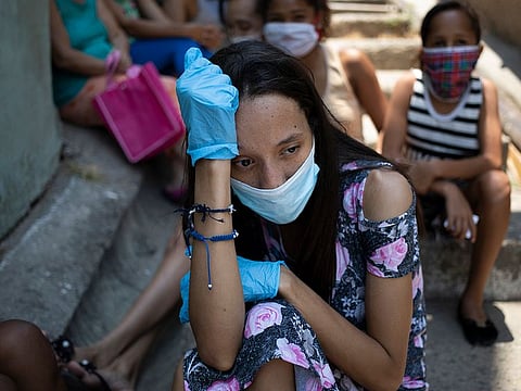 A woman wearing a protective face mask and disposable gloves as a measure to curb the spread of the new coronavirus, waits outside a soup kitchen, in Caracas' Petare slum in Venezuela, Thursday, April 30, 2020.