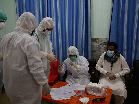 Health officials in protective gear take a sample from a man at a screening and testing facility for COVID-19 in Peshawar, Pakistan, Wednesday, June 3, 2020.