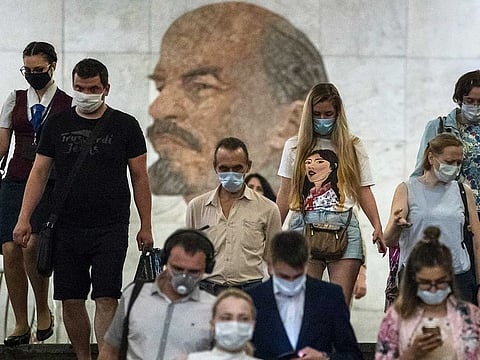 People wearing face masks to protect against coronavirus walk through the subway, with a portrait of Soviet founder Vladimir Lenin in the background, in Moscow, Russia, Wednesday, June 10, 2020. Moscow residents are no longer required to stay at home or obtain electronic passes for travelling around the city.
