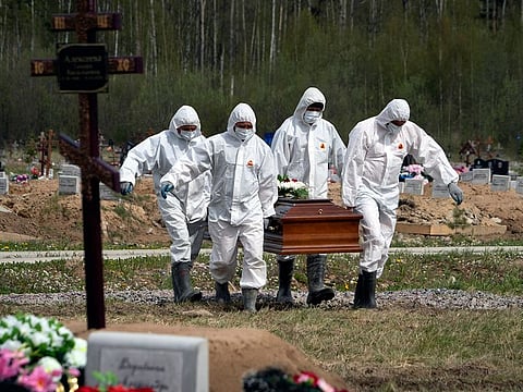 Gravediggers in protective suits carry the coffin of a COVID-19 victim as relatives and friends stand at a distance in the section of a cemetery reserved for coronavirus victims in Kolpino, outside St. Petersburg, Russia. A WHO report has found crucial flaws in the global response in early 2020 to the COVID-19 outbreak.