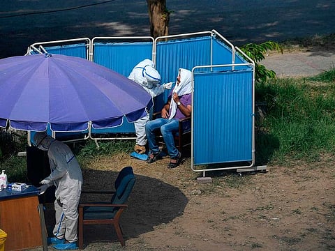 A health official (top L) wearing personal protective equipment (PPE) takes a sample from a man sitting in a temporary cabin at a drive-through screening and testing facility for the COVID-19 coronavirus, alongside a street in Islamabad on June 7, 2020.