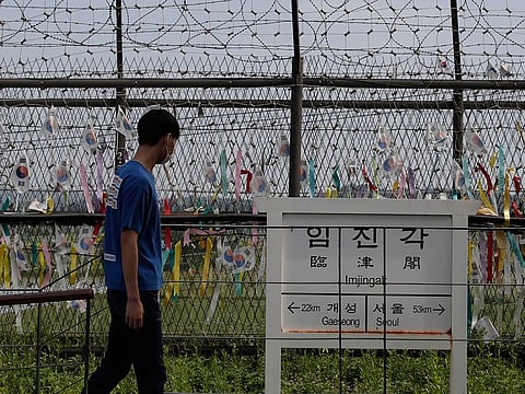 A visitor walks in front of a directional sign showing the distance to North Korea's Kaesong city and South Korea's capital Seoul near the wire fences decorated with ribbons written with messages wishing for the reunification of the two Koreas at the Imjingak Pavilion in Paju, South Korea, Sunday, June 14, 2020.