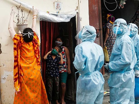 A woman rolls up a protective sheet at the entrance of a house so healthcare workers wearing personal protective equipment (PPE) can check the temperature of residents during a check-up camp for the coronavirus disease (COVID-19) in Mumbai, India June 17, 2020.