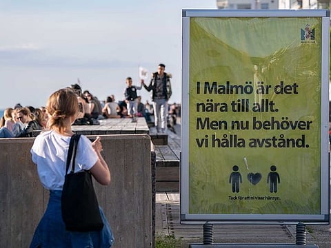 People enjoy the warm evening weather in Malmo, Sweden, Tuesday May 26, 2020 as a sign reads 'In Malmo everything is near. But now we need to keep a distance'. Sweden has defended its response to the COVID-19 global pandemic despite the country now reporting one of the highest mortality rates in the world with 4,125 fatalities, about 40 deaths per 100,000 people.