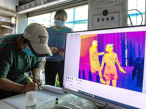 Customers sign in and have their temperatures checked by thermal imaging before entering a market in Beijing on June 20, 2020.
