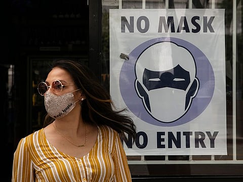 File picture: A woman walks out of a liquor store past a sign requesting its customers to wear a mask, in Santa Monica, California.