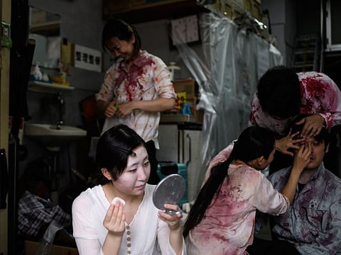 This picture taken on June 15, 2020 shows drive-in haunted house actress Haruna Suzuki (front L), 20, putting on zombie makeup before a demonstration of a drive-in haunted house at a garage in Tokyo.
