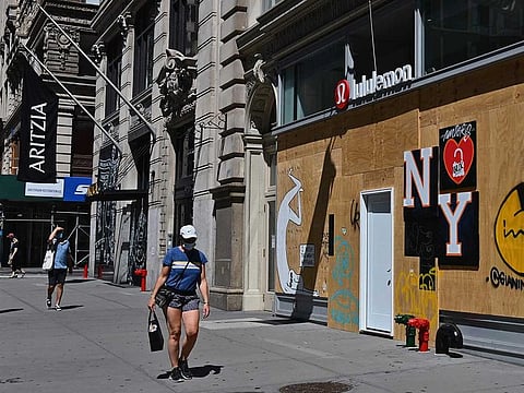 A woman wearing a face mask walks past a boarded up Lululemon shop on Broadway in the SoHo neighborhood of Manhattan on June 24, 2020 in New York City.