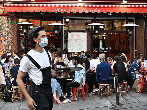 A waiter wearing a face mask serves clients while people eat and have drinks on the terrace of the cafe-restaurant "Le Bar du Marche" in Paris as cafes and restaurants reopen in France with the easing of lockdown mesures taken to curb the spread of the COVID-19 pandemic, caused by the novel coronavirus.