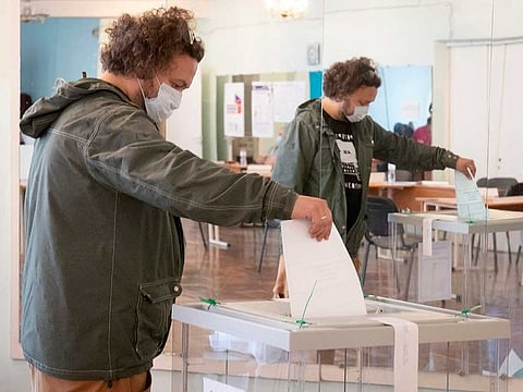 A man wearing a face mask to protect against coronavirus infection reflects in a mirror as he casts his ballot at a polling station in St.Petersburg, Russia, Wednesday, July 1, 2020.