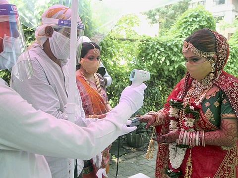 A security guard uses a thermal screening device on Heli, the bride, as she arrives for her wedding ceremony, at a marriage hall in Mumbai, Thursday, June 25, 2020