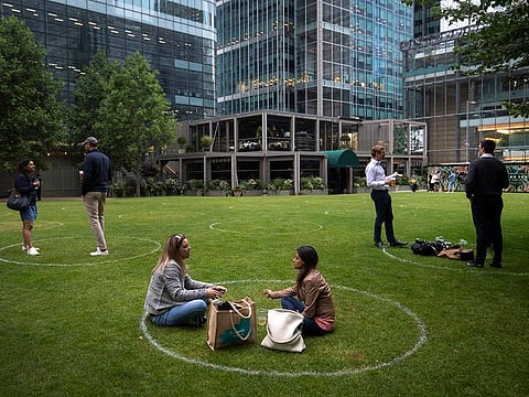 People stand within rings marked on the grass to maintain their social distance outside a bar in Canary Wharf, East London as further coronavirus lockdown restrictions are lifted in England, on Wednesday, July 1, 2020.
