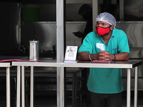 A restaurant worker wearing a face mask as a precaution against coronavirus holds a thermometer as he waits to serve takeaway food to customers during lockdown in Bengaluru, India, Sunday, July 5, 2020.
