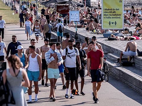 An information sign recommends people to keep social distance due to the coronavirus disease (COVID-19) pandemic, where people stroll, sunbathe and swim at a bathing jetty during a heatwave in Malmo, Sweden, on June 25, 2020.