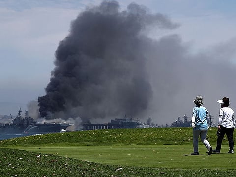 Golfers play on as a fire burns on the amphibious assault ship USS Bonhomme Richard at Naval Base San Diego on July 12, 2020 in San Diego, California.