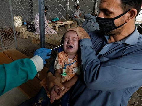 A paramedic wearing protective gloves takes a nasal swab from a baby, to be tested for the coronavirus disease, in Karachi, Pakistan.