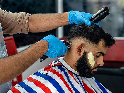 A hairdresser wearing a face mask, due to the COVID-19 pandemic, cuts a customer's hair.