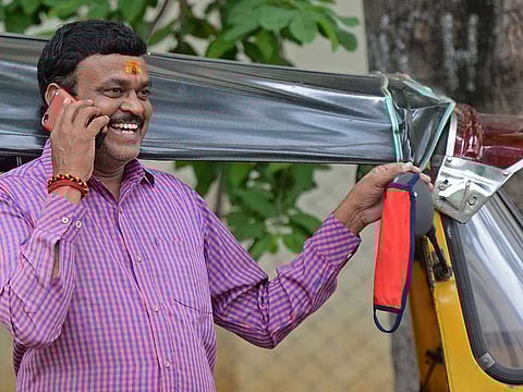 In this picture taken on July 9, 2020, Srinivas, an auto-driver speaks on a mobile phone as he hangs his facemask on the side mirror of his parked auto during the COVID-19 coronavirus pandemic, in Hyderabad. Indian police are having a field day handing out fines to people who do not wear a mask during the coronavirus pandemic.