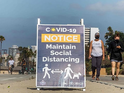 Women wearing facemasks walk near a notice about maintaining social distance on the beach in Long Beach, California, on July 14, 2020.