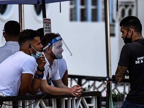 A waiter covers his face with a shield as he chats with another man at a restaurant on Ocean Drive in Miami Beach, Florida on July 14, 2020, amid the coronavirus pandemic. A top Swiss doctor has asked restaurants not to rely on plastic visors to protect their employees.
