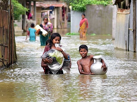 Children wade through floodwaters carrying essential utensils to take shelter at a safe place after their houses were submerged in at Shimlitola village under Goalpara district, in Guwahati on Tuesday.