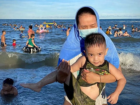 A woman wearing a mask carries her child on a beach in Vung Tau city, Vietnam, Sunday, July 26, 2020. Vietnam on Sunday reimposed restrictions in one of its most popular beach destinations after a second person tested positive for the virus, the first locally transmitted cases in the country in over three months.
