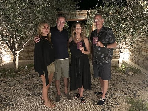 In this photo provided by Greek Prime Minister's Office, Greek Prime Minister Kyriakos Mitstotakis, second left, his wife Mareva Grabowski-Mitsotaki, left, pose next to US actor Tom Hanks, right, and his wife Rita Wilson holding up their new Greek passports, in the island of Antiparos, Greece on Saturday, July 25, 2020.