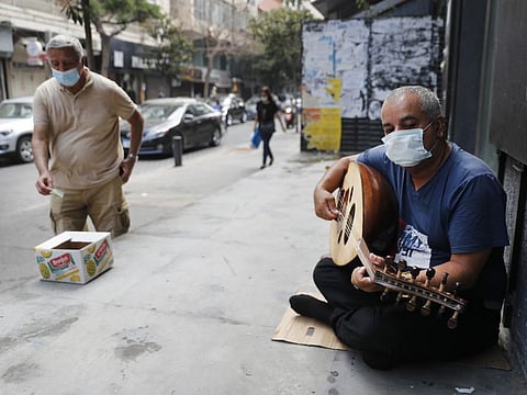 A street musician man performs with a mask on his face to help stop the spread of the coronavirus, as other man on the left puts money on a box, in Beirut, Lebanon, Wednesday, July 29, 2020. Lebanon is hurtling toward a tipping point at an alarming speed, driven by financial ruin, collapsing institutions, hyperinflation and rapidly rising poverty _ with a pandemic on top of that. The collapse threatens to break a nation seen as a model of diversity and resilience in the Arab world.