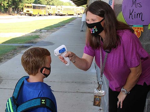 In a photo provided by Newton County Schools, teaching assistant Crystal May talks to kindergarten student Lewis Henry Thompson, 5, as she takes his temperature at Newton County Elementary School in Decatur, Miss., Monday, Aug. 3, 2020.