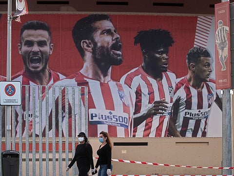 FILE: two women wearing face masks pass by a giant poster of Atletico Madrid players at the Wanda Metropolitano stadium in Madrid, Spain in May 2020.