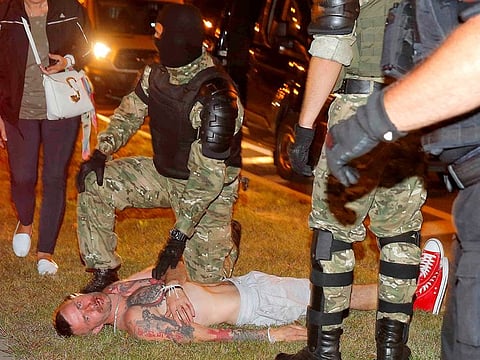 A law enforcement officer kneels next to a man laying on the ground during clashes with opposition supporters after polls closed at the presidential election in Minsk, Belarus, August 9, 2020.