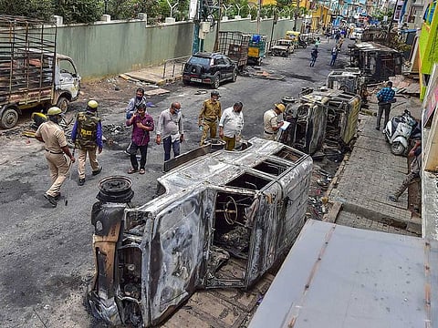 Police and residents walk past charred remains of vehicles vandalised by a mob over a social media post, allegedly by a relative of a Congress MLA, in Bengaluru, Wednesday, Aug. 12, 2020. Atleast three people were killed after police opened fire to quell a mob.