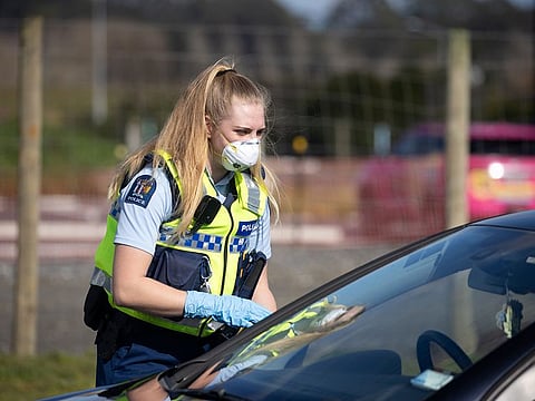A police officer wearing a protective mask talks to a motorist at a checkpoint in the Bombay area of Auckland, New Zealand, on Wednesday, Aug. 12, 2020.