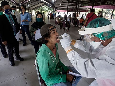 A medical worker takes the nasal swab sample from a man as others queue up for their turn, during a mass test for the new coronavirus in Medan, North Sumatra, Indonesia, Tuesday, Aug 18, 2020.