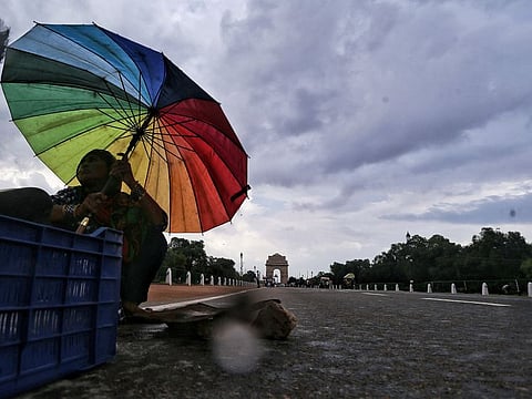 A woman covers herself with an umbrella during the rain at India Gate, Rajpath in New Delhi on Sunday