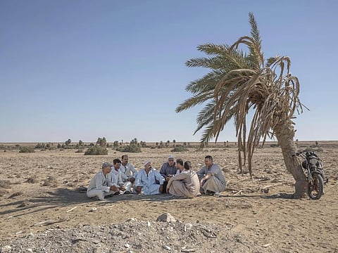 55-year-old Egyptian farmer Makhluf Abu Kassem, center, sits with farmers under shade of a dried up palm tree surrounded by barren wasteland that was once fertile and green, in Second Village, Qouta town, Fayoum, Egypt, Wednesday, Aug. 5, 2020. Abu Kassem fears that a dam Ethiopia is building on the Blue Nile, the Nile's main tributary, could add to the severe water shortages already hitting his village if no deal is struck to ensure a continued flow of water