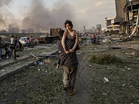 In this August 4, 2020 file photo, Hoda Kinno, 11, is evacuated by her uncle Mustafa, in the aftermath of a massive explosion at the port in Beirut, Lebanon. The Kinno family from Syria's Aleppo region was devastated in the wake of the explosion - Hoda suffered a broken neck and other injuries and her sister Sedra, 15, died in the explosion.