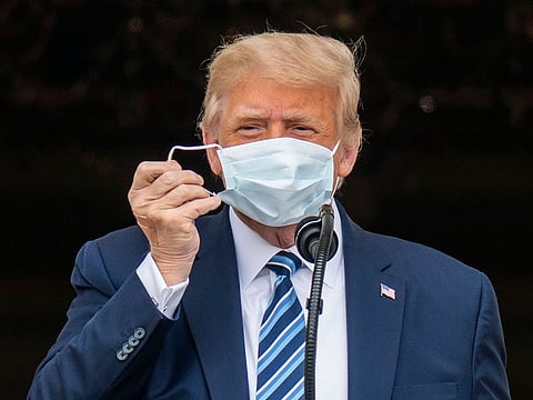 President Donald Trump, with an adhesive bandage on his right hand, takes off his face mask while on the balcony of the White House in Washington, during a rally Saturday, Oct. 10, 2020, his first public event since being hospitalized for COVID-19.