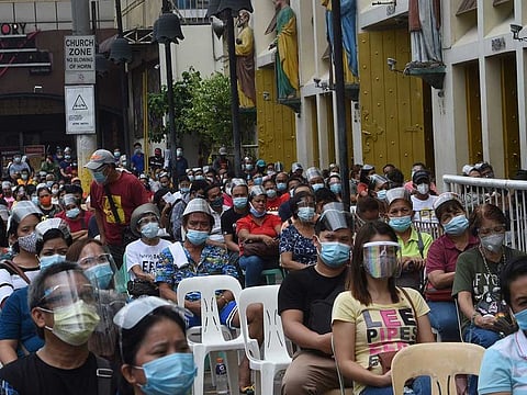 Catholic faithful sit outside the Quiapo church in Manila on October 9, 2020, as health protocols imposed by authorities limit church goers inside the church to filling only 10 percent of their seating capacity.