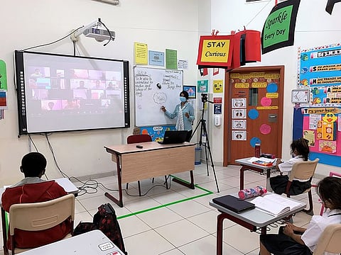 A teacher attending to both in-class and at-home students from a hybrid classroom at Credence High School, Dubai.